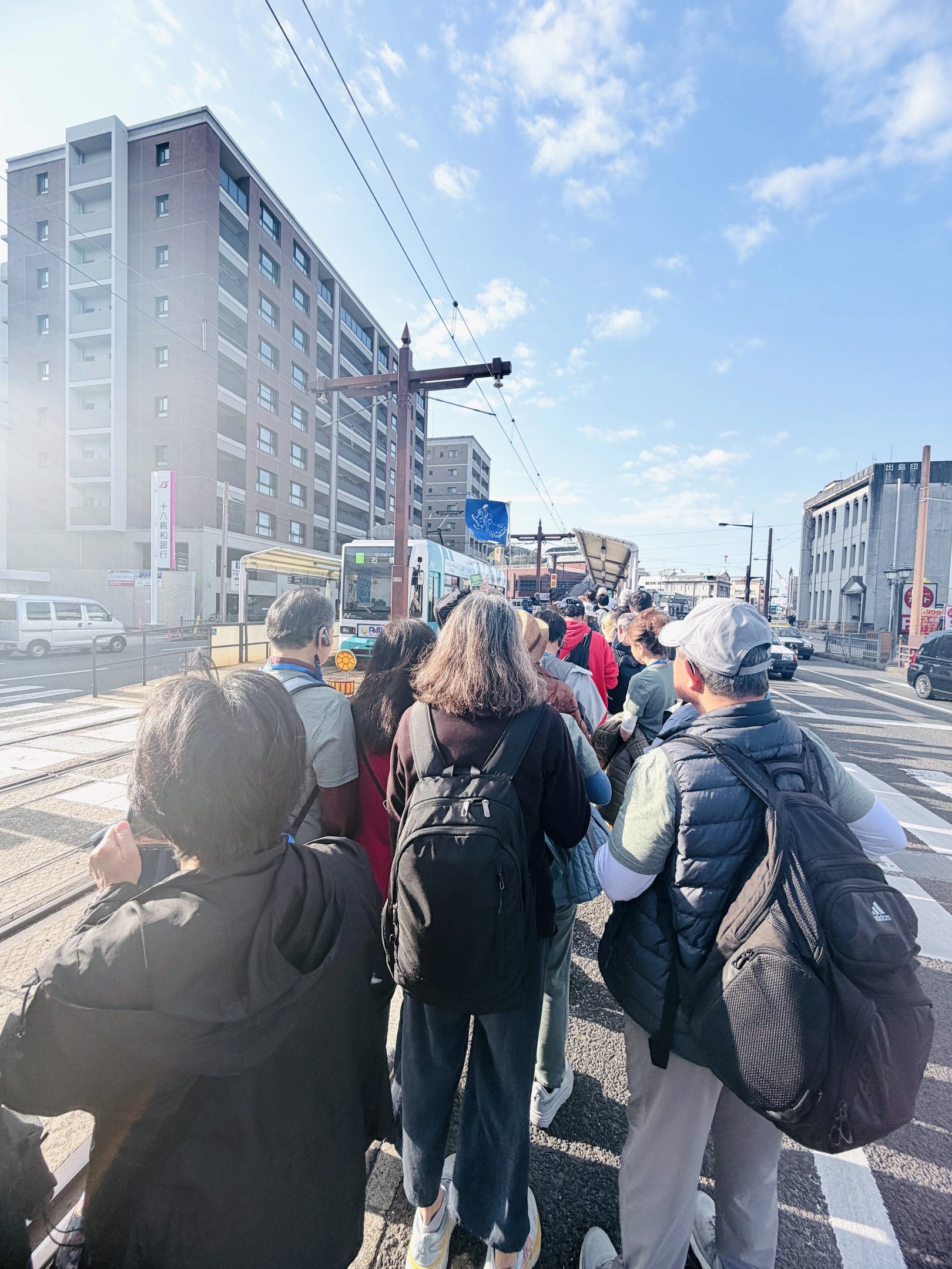 Crowded tram stop in Nagasaki with many tourists waiting to board during peak travel time