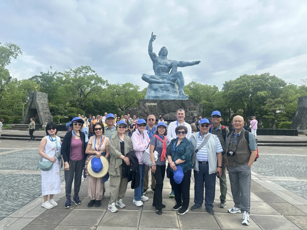 A group of 13 Vietnamese tourists posing for a commemorative photo in front of the Peace Statue in Nagasaki, Japan.