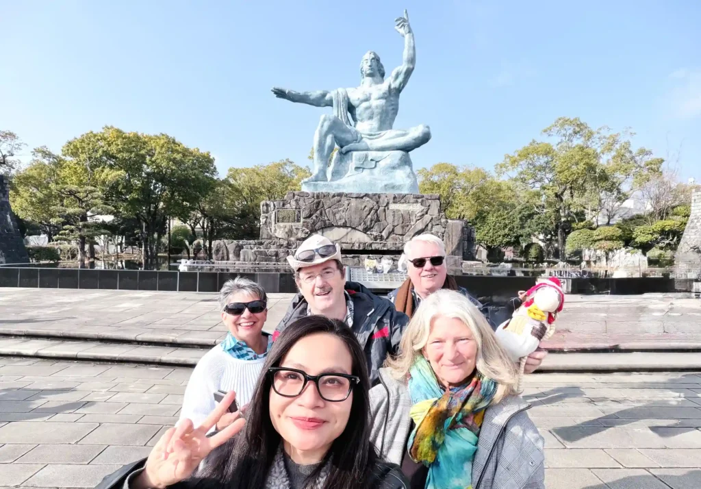 A local guide taking a selfie with guests in front of the Peace Statue at Nagasaki Peace Park.